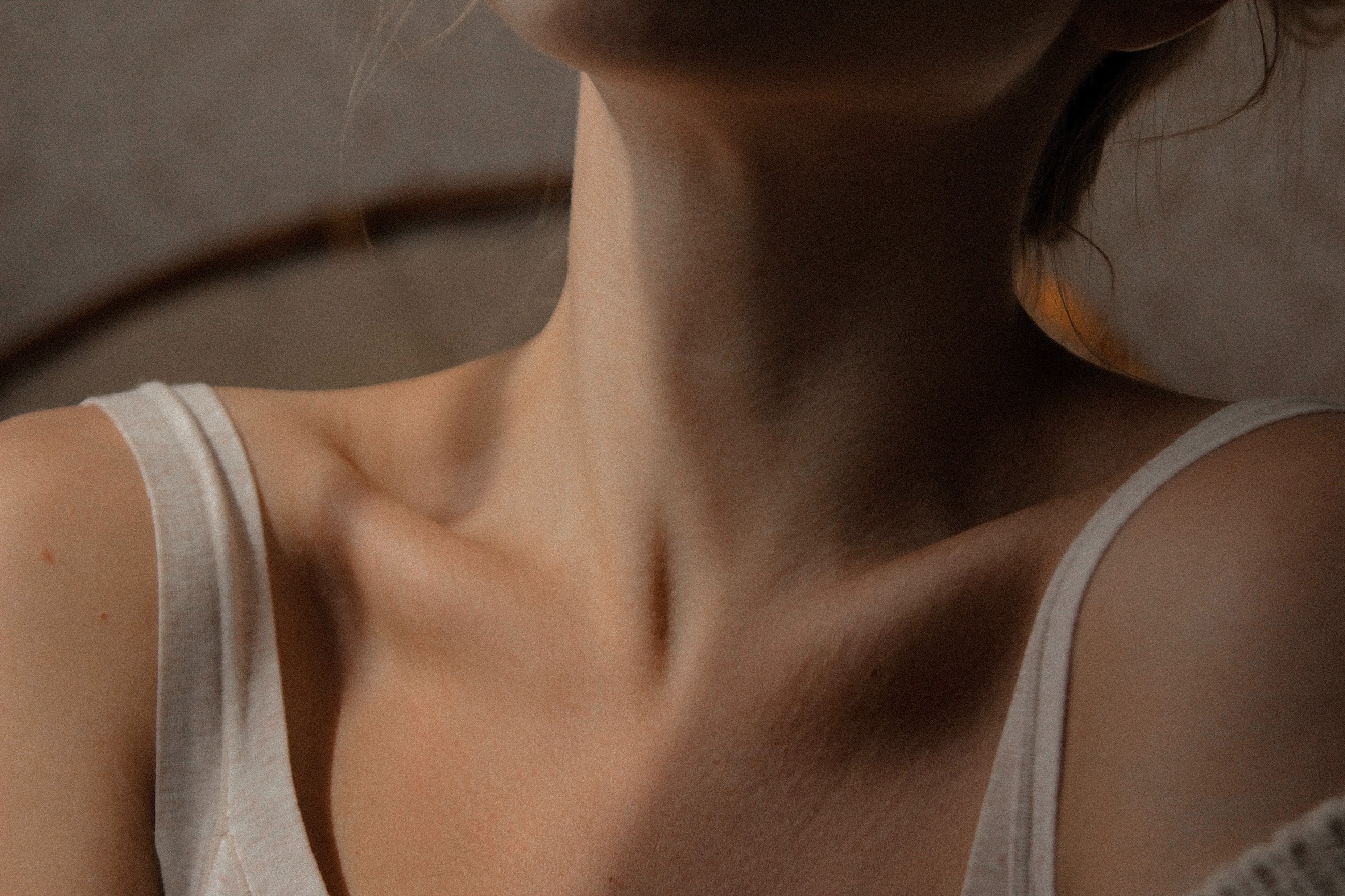Close editorial view of a neck and collarbones in soft natural light, with white linen straps