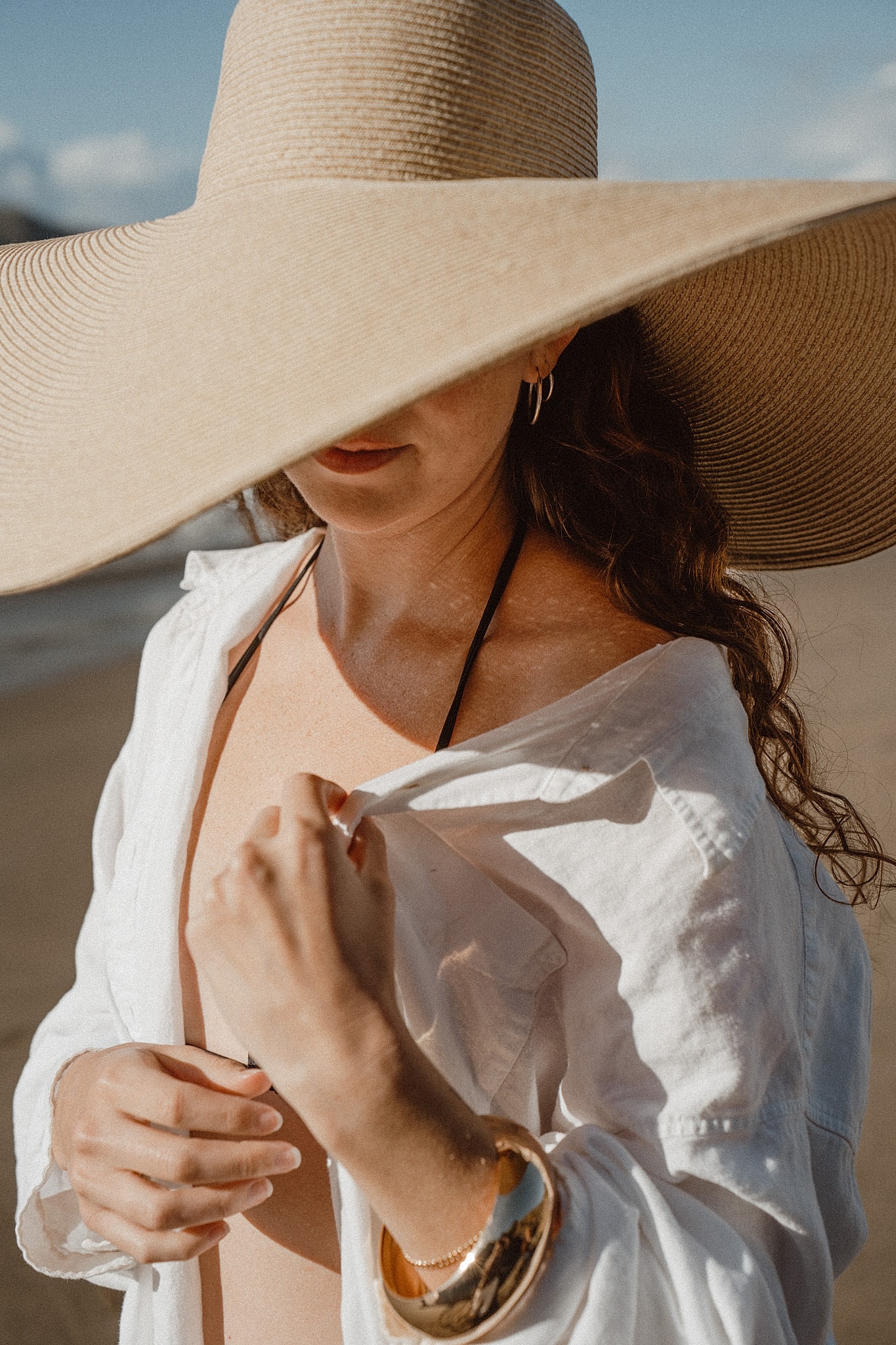 Woman in a wide-brimmed straw hat and open white shirt by the sea