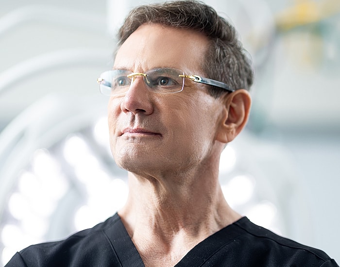 Male medical professional in surgical attire, thoughtful expression.