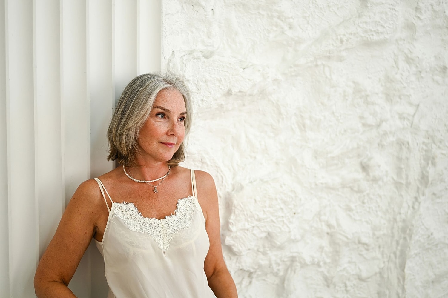 Confident older woman with gray hair looking out window, representing women considering breast reduction surgery later in life