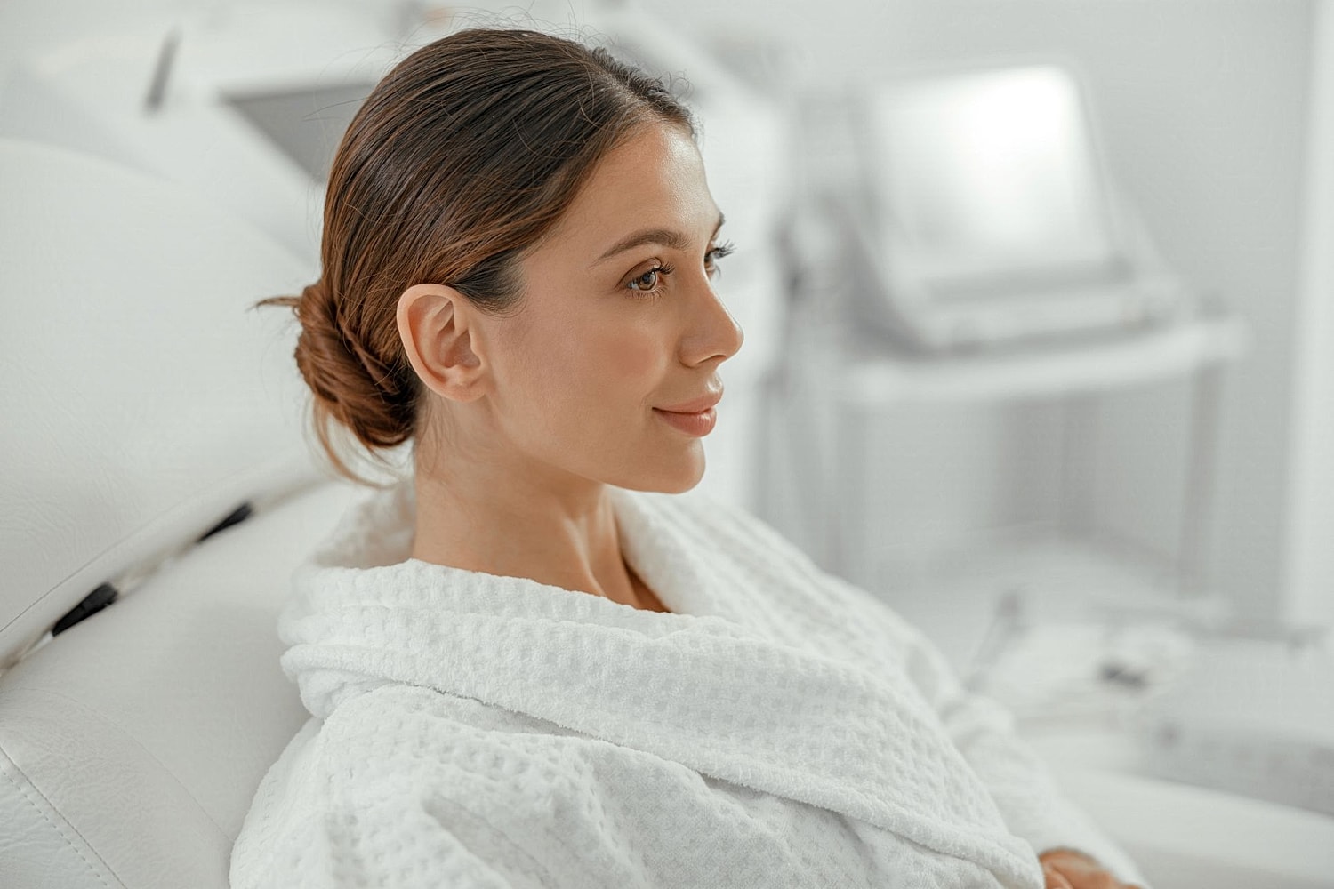 Woman in a white robe relaxing in a bright med spa treatment room before an aesthetic consultation.