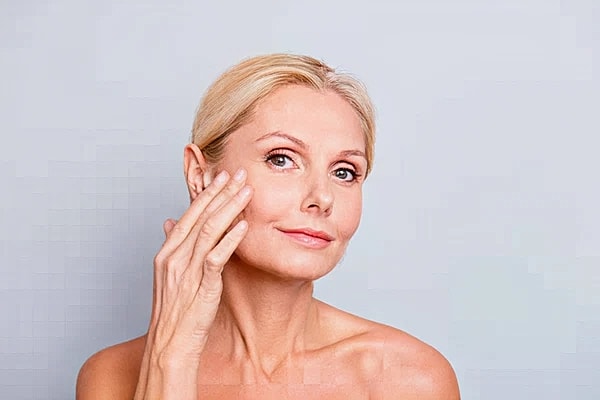 A woman touching her cheek and showing the results of Thermage® FLX treatments