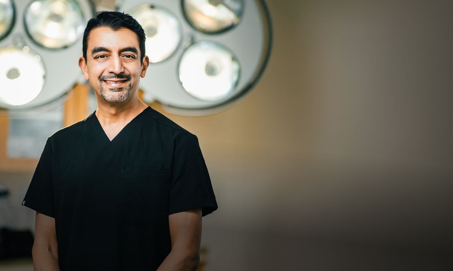 St. Louis facial plastic surgeon, Dr. Nayak smiling in operating room setting.