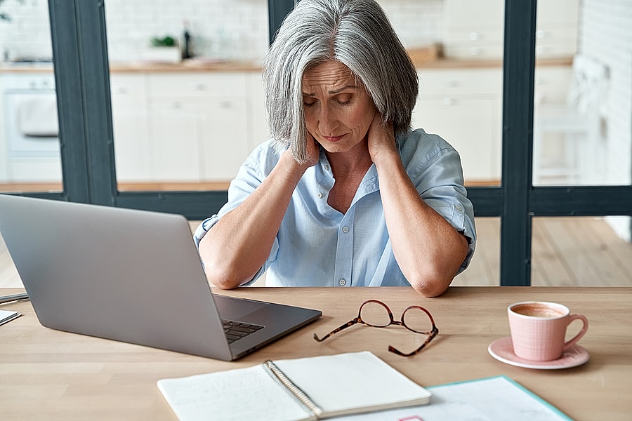 whiplash victim working on laptop at home and holding her neck