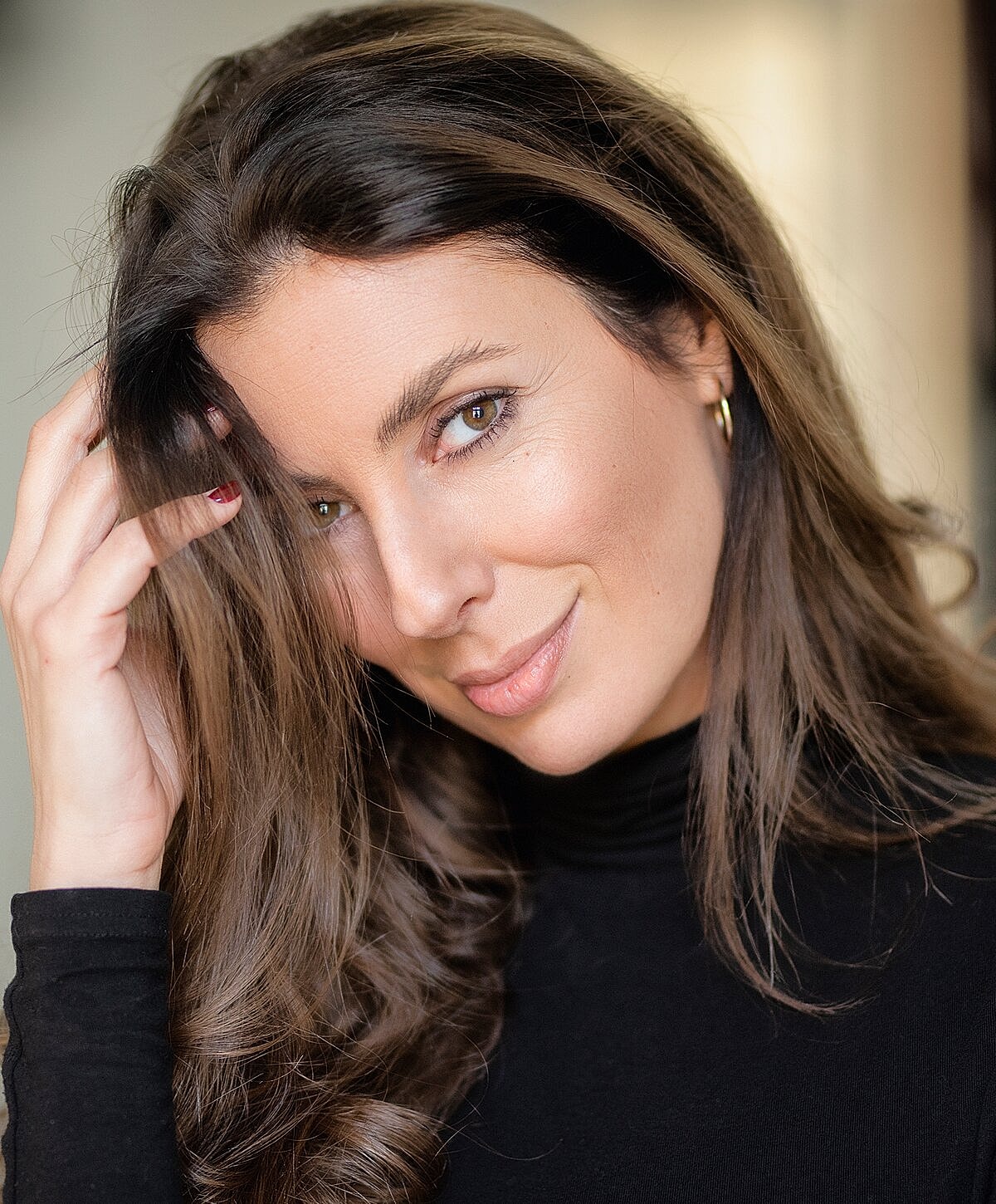 Woman with long hair posing thoughtfully in black top.