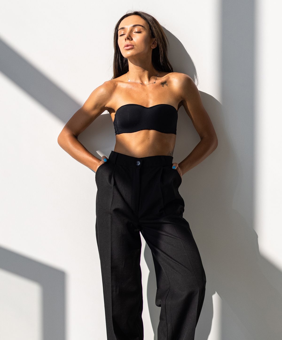 Woman in black outfit posing against a wall.