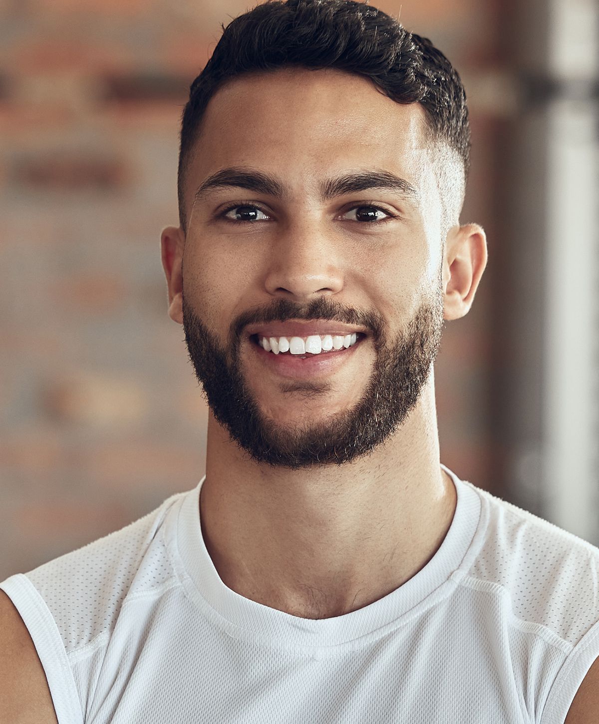 Smiling man with muscular physique, hands on head.