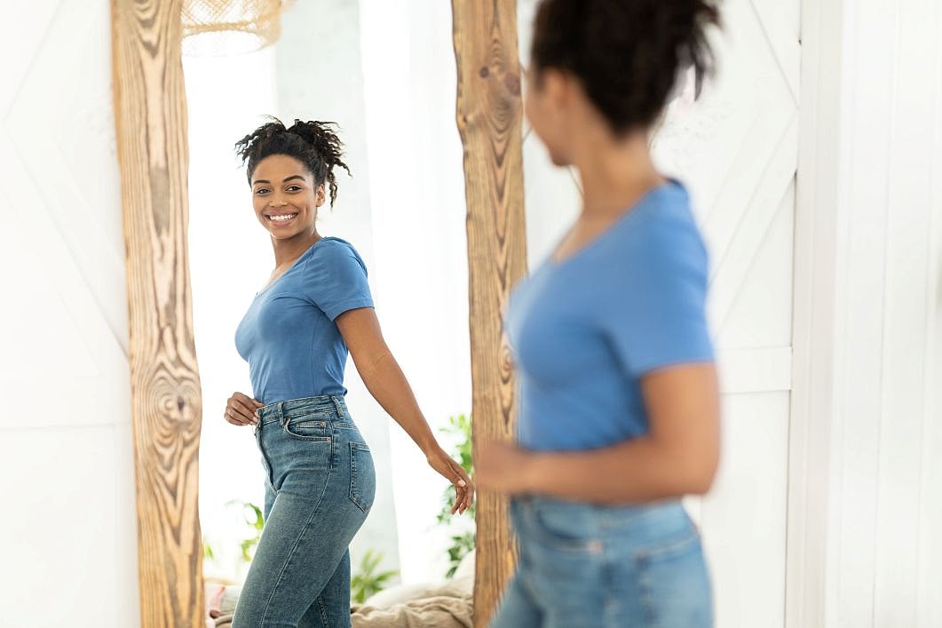 Woman smiling at her reflection while examining body shape after significant weight loss