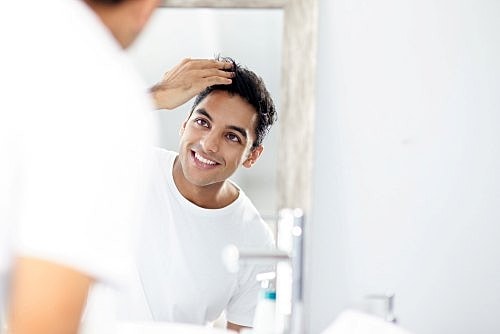 Man smiling in the mirror running a hand through his hair